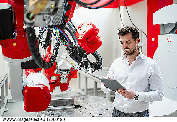Young man using digital tablet by robotics in factory