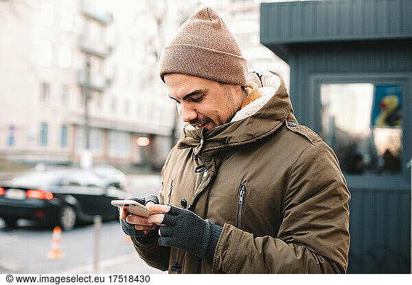 Young man using smart phone standing on street in city in winter