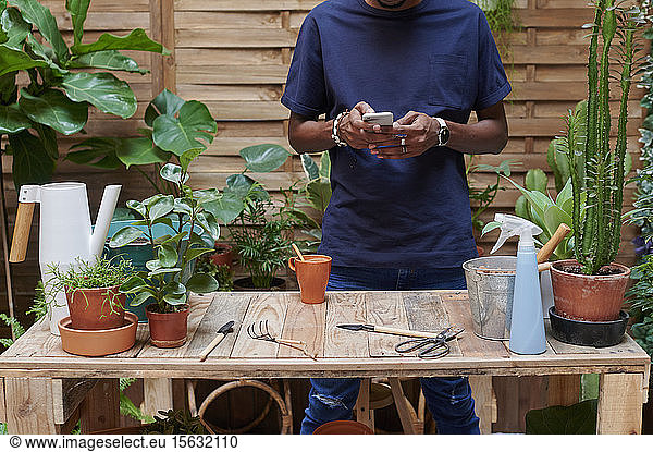 Young man using smartphone on his terrace while gardening