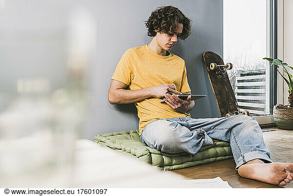 Young man using tablet PC by skateboard at home