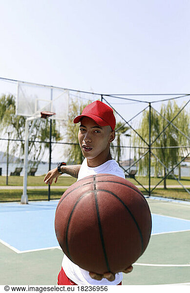 Young man wearing cap holding basketball at sports court