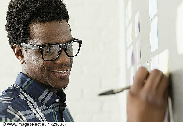 Young man wearing glasses writing on adhesive note