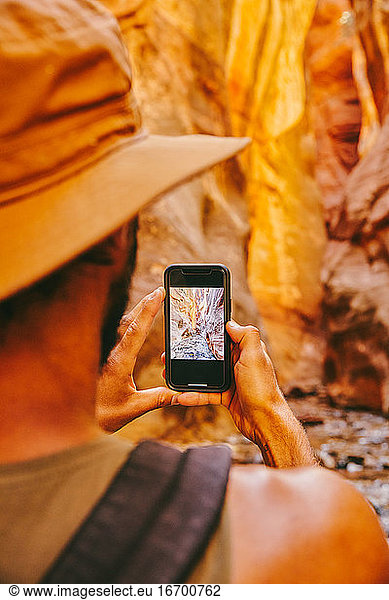 Young man wearing hat taking picture of slot canyons in Kanarra Falls