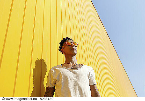 Young man wearing red sunglasses in front of yellow wall