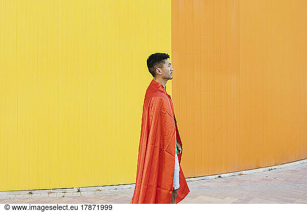 Young man wearing red superhero cape standing in front of wall