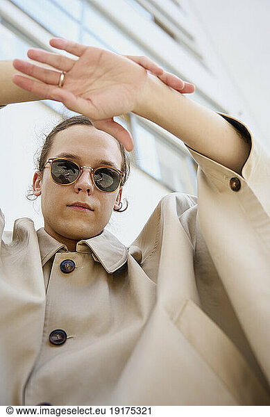 Young man wearing sunglasses and gesturing near building