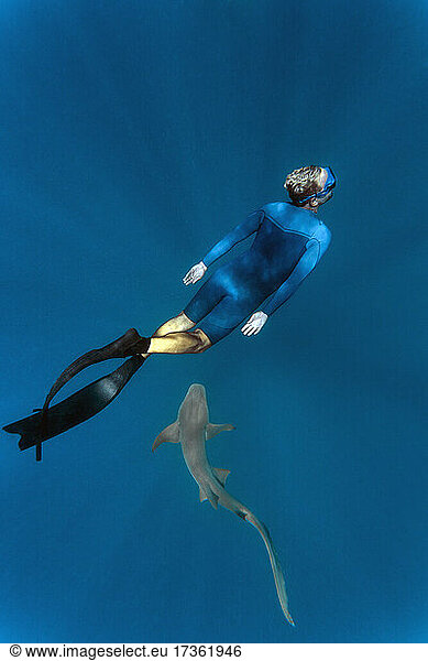 Young man wearing wet suit snorkeling with nurse shark in sea