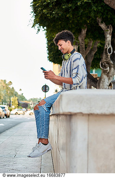Young man with afro hair smiles while he is using his smartphone