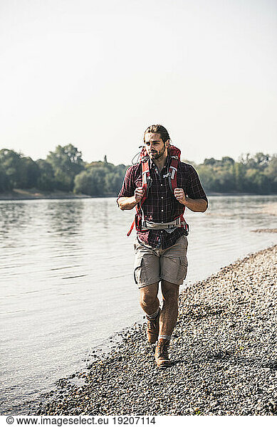 Young man with backpack walking at the riverside