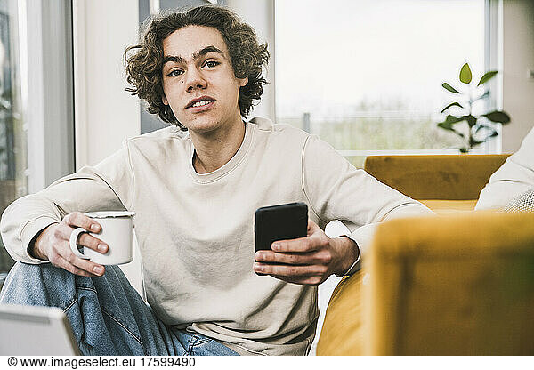 Young man with coffee cup and smart phone at home