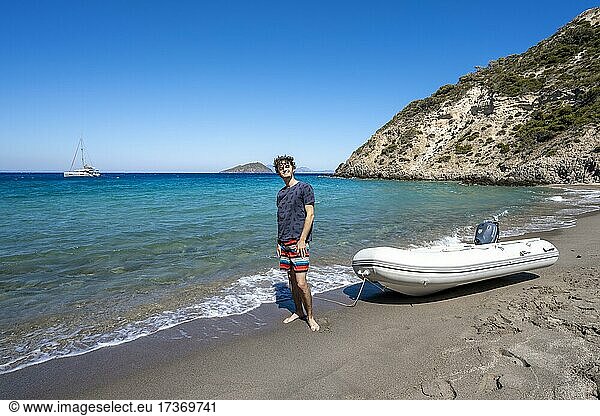 Young man with dinghy on a beach in Gyali  sailing boat behind  Dodecanese  Greece  Europe