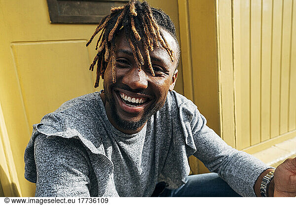 Young man with dreadlocks laughing in front of building