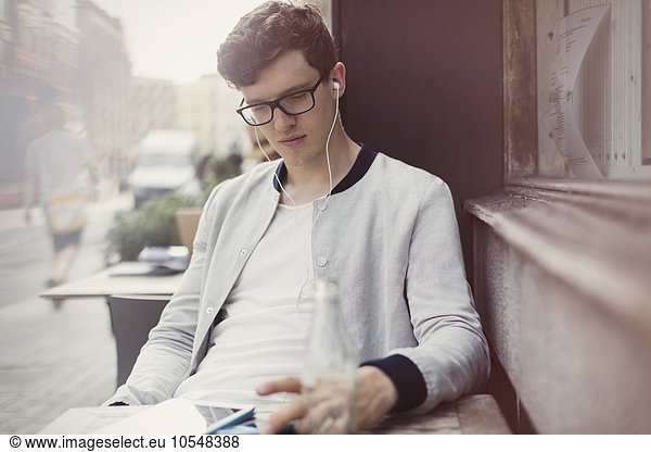 Young man with eyeglasses and headphones using digital tablet at sidewalk cafe