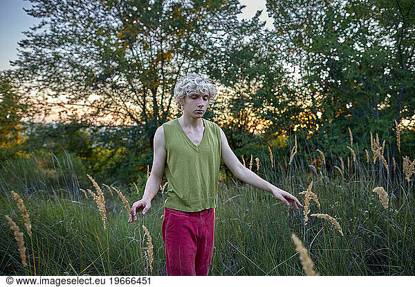 young man with eyes closed eyes walks among grass