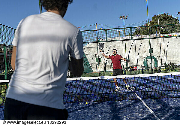 Young man with friend playing paddle tennis at sports court on sunny day