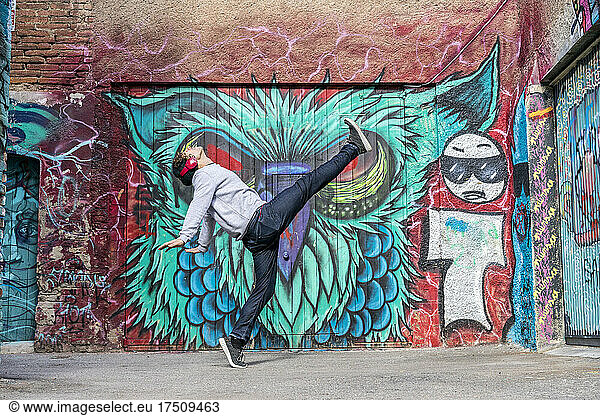 Young man with headphones dancing in font of graffiti