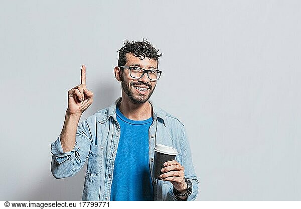 Young man with paper coffee cup pointing finger up  Happy smiling person with paper coffee cup pointing finger up
