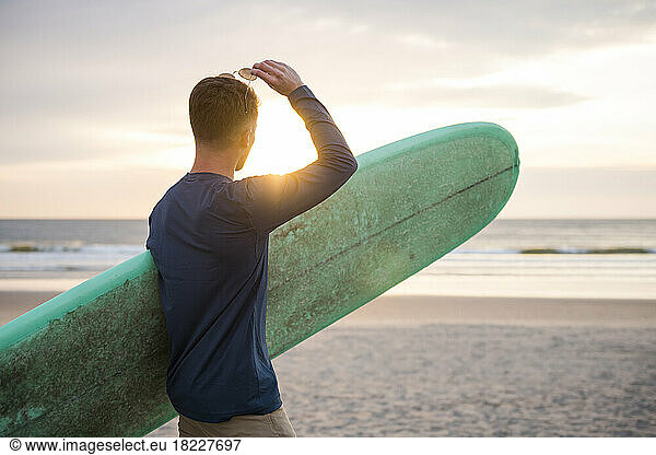 Young Man with sunglasses and surfboard at sunrise at Beach