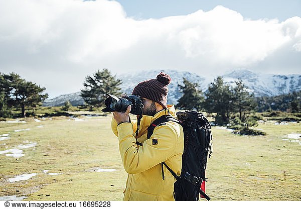 Young man with yellow jacket and backpack taking pictures on the mount