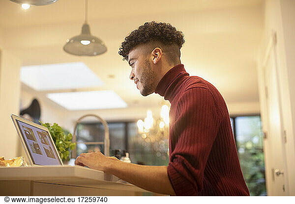 Young man working from home at laptop in kitchen