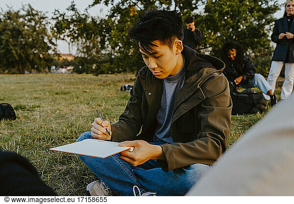 Young man writing in book at park