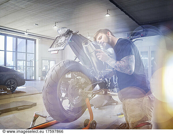 Young mechanic examining exhaust pipe of motorcycle in workshop