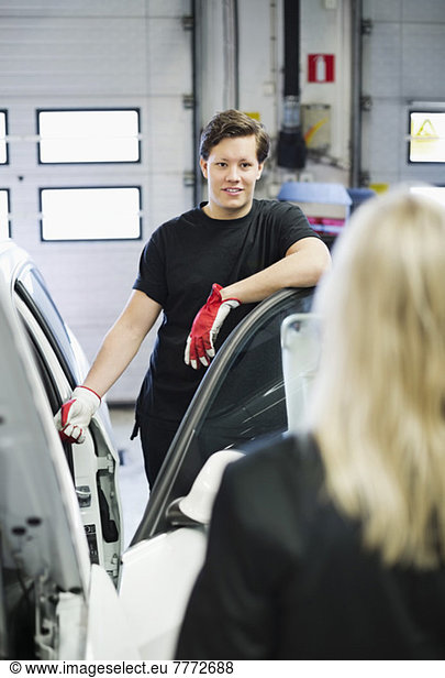 Young mechanic looking at female customer while standing by car in auto repair shop