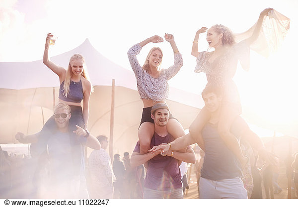 Young men carrying playful women on shoulders at music festival