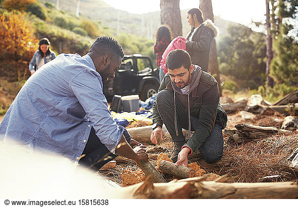 Young men friends building campfire at campsite