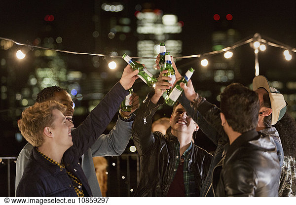 Young men toasting beer bottles at rooftop party