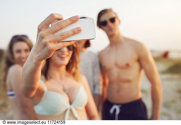 Young men  young woman and teenage girl (16-17) taking selfie on beach
