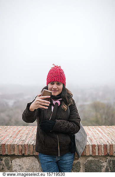 Young Mexican woman with wool hat taking a selfie on a foggy day
