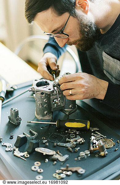 Young millennial mechanic man taking apart carburetor for restoration