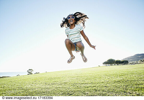 Young mixed race girl with long curly hair leaping in the air