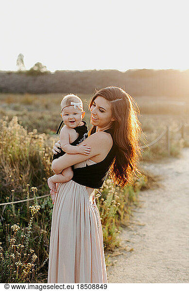 young mom and happy baby girl snuggling in sunset