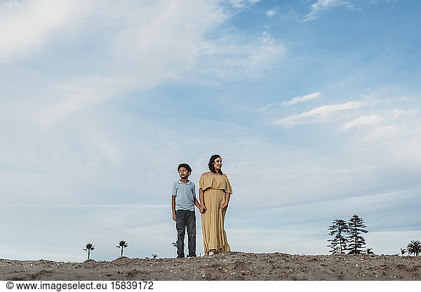 Young mother and school-aged son standing on beach dune