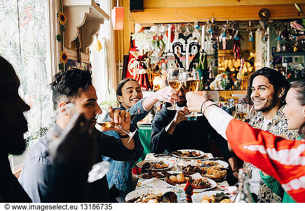 Young multi-ethnic friends enjoying while raising toast at table in restaurant