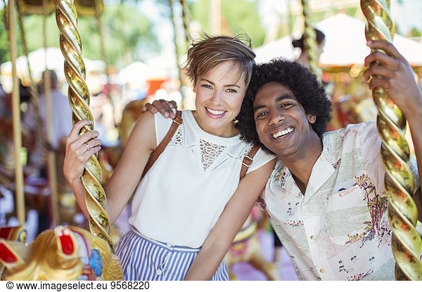 Young multiracial couple smiling on carousel in amusement park