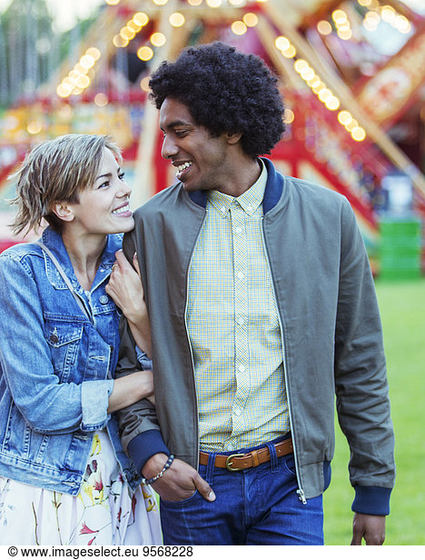 Young multiracial couple smiling to each other in amusement park
