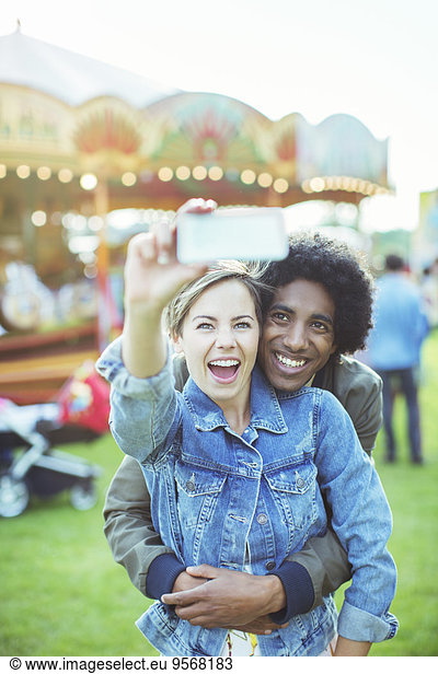 Young multiracial couple taking selfie in amusement park