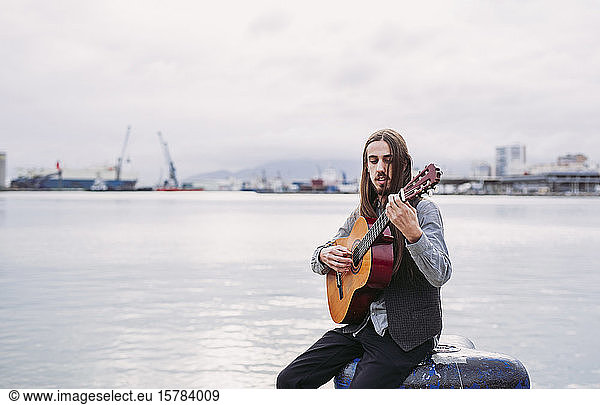 Young musician playing guitar at the port