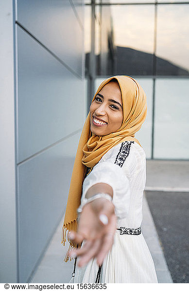 Young muslim woman smiling  wearing yellow hijab and giving her hand