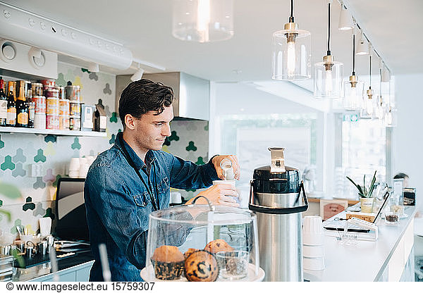 Young owner making coffee at checkout counter in office cafe