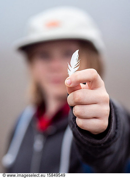 Young person holding small feather at arms lenght