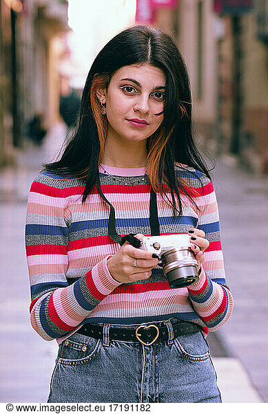 Young photographer poses on a city street with the camera in her
