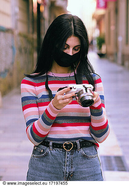 Young photographer with anti virus mask using her camera on a ci