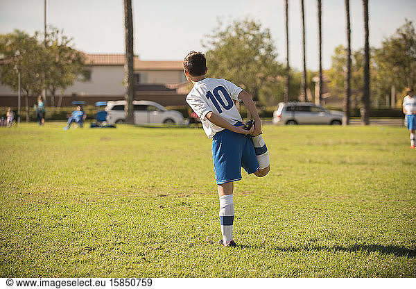 Young player in soccer uniform streching in the park