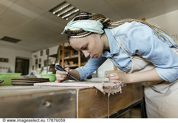 Young potter with hand tool working at art studio
