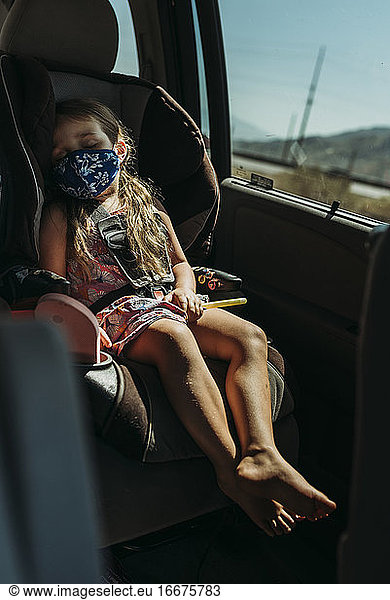 Young preschool aged girl with mask on taking nap in car on vacation