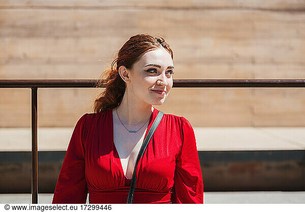 Young red-haired woman enjoying the sun in the city. Dressed in a red blouse.